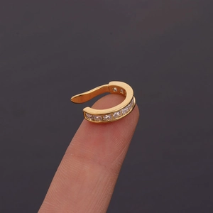Close-up of golden U-shaped ear clip with square zirconias held on a fingertip