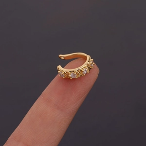Close-up of a gold X-shaped ear cuff with sparkling zircons held on a fingertip