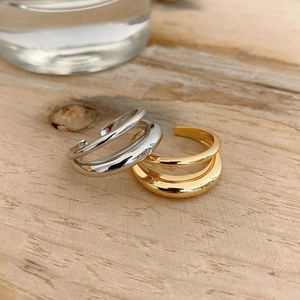 Detail of minimalist double-layered wavy open rings in gold and silver on wood