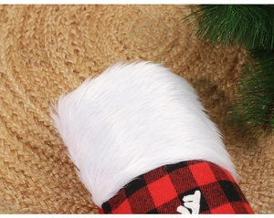 Close-up of red and black plaid Christmas stocking with white faux fur trim and pine needle