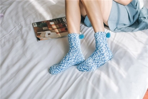 Close-up of blue coral fleece socks with fluffy pompoms on white bedding background