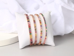 Detailed view of four colorful rainbow zircon tennis bracelets on a white jewelry pillow