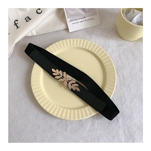 Detail of a black elastic waist belt with an elegant gold leaf-shaped metal buckle on a plate