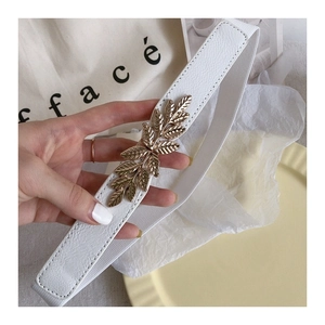 Close-up of a white elastic waist belt featuring a gold leaf-shaped metal buckle design