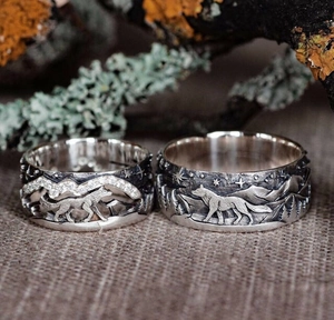 Detalle de anillos de lobo vintage con grabados de montaña sobre fondo de musgo rural