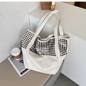 Detailed view of white leather tote bag with vintage metal stud rivets in a grid pattern