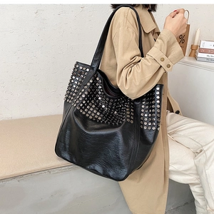 Detailed view of large black tote bag with silver studs worn by a model in soft light