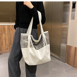Detailed view of large white tote bag with black rivets on model in modern setting