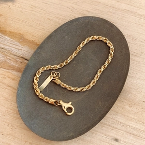 Detailed close-up of a 925 sterling silver gold twisted rope bracelet on textured stone
