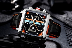 Macro detail of square mechanical watch dial with luminous hands and orange accents