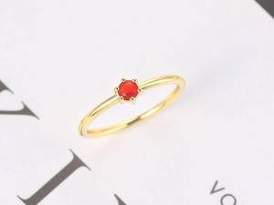 Macro shot of minimalist gold ring with a red round gemstone in a six-prong setting
