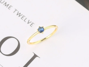 Macro detail of six-prong setting with a round blue gemstone on a gold slender band
