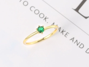 Macro shot of minimalist gold plated six-prong ring with a round green gemstone