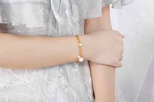 Close-up of a double-layer gold pearl bracelet worn by a model in a grey dress