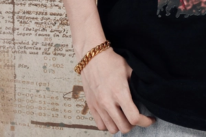 Primo piano di un bracciale a catena cubana dorata al polso su uno sfondo di carta vintage