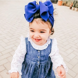 Toddler model wearing a navy blue ribbed large bow headband and denim outfit outdoors