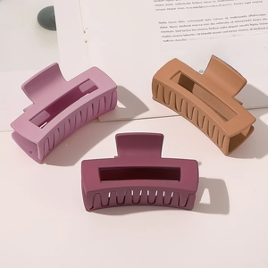 Three matte rectangular hair claws in purple, brown, and burgundy on a magazine