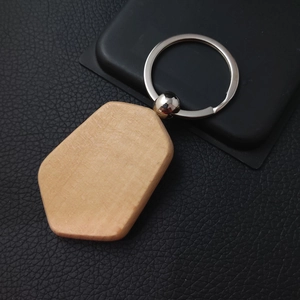 Close-up of pentagon beech wood keychain with metal ring on black leather surface