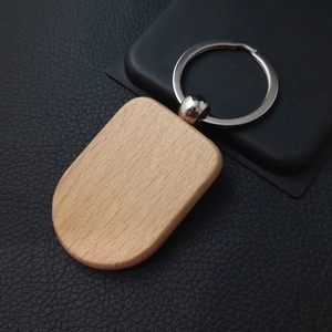 Detailed top view of a blank oval beechwood keychain with metal ring on black leather texture