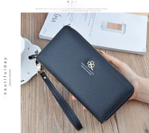 Detail view of lychee pattern leather wallet with gold clover logo and wrist strap