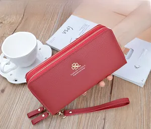 Macro shot of red pebble leather wallet featuring dual gold zippers and a wrist strap
