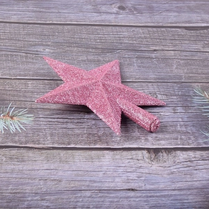 Sparkly pink glitter Christmas tree topper star with a cylindrical base on a wooden background