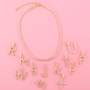 Collier tennis doré avec pendentifs lettres en strass sur un fond rose vif élégant