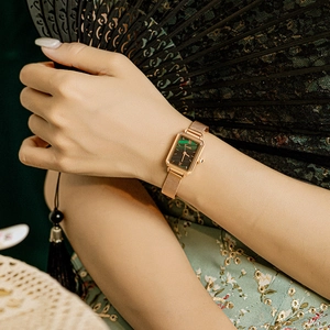 Elegant gold mesh strap watch with deep green rectangular dial shown on woman's wrist