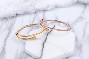 Detail of twisted steel cable bangles in gold and rose gold on a marble display