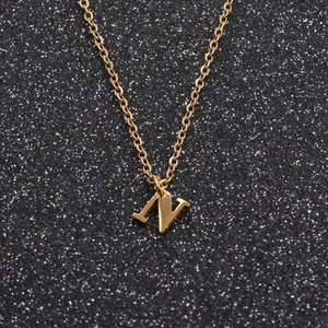 Close-up of golden geometric necklace featuring a polished letter N pendant on black background