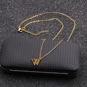 Detail of a golden chain necklace featuring a geometric letter W pendant on a dark surface