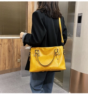 Litchi texture yellow handbag shown on shoulder in a modern urban elevator setting