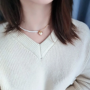 Close-up of pearl and gold chain necklace with a heart pendant on a woman neck