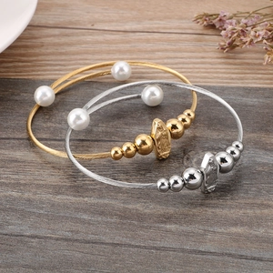 Goldene und silberne Spiral-Armreifen mit Perlen und Anhängern auf Holzoberfläche