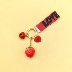 Detail of red strawberry keychain with metal bell, love ribbon and gold heart charm