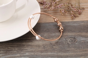 Detail view of rose gold layered bangle with pearls and sparkling zircon on wood surface