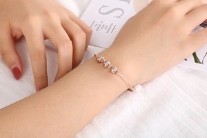 Detail of rose gold bangle featuring a pearl and zircon balls on a model wrist