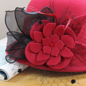 Close-up of elegant red wool felt hat with handcrafted flower, black mesh, and feathers