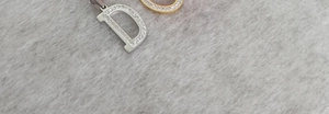 Detailed view of D-letter pendants in gold and silver steel with cubic zirconia