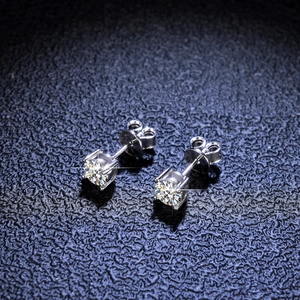 Macro shot of silver four-prong moissanite stud earrings on a dark blue leather background