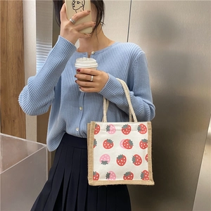 Detail of canvas lunch bag with strawberry print and jute handles held by a model