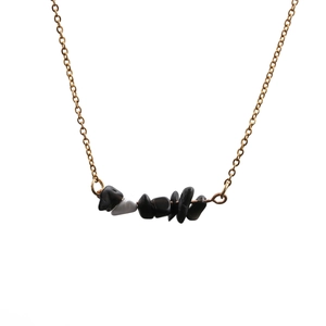 Flat lay of a gold link necklace with black and grey irregular stone pendants on white background