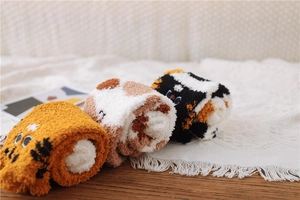 Three pairs of rolled fluffy cat-patterned coral fleece socks on a white fringed rug