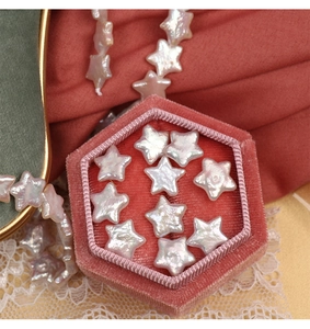 Close-up of star-shaped freshwater pearls in a pink velvet box on red silk background