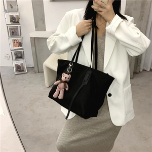 Close-up of black tote bag with pink knit bear charm worn by a model in studio
