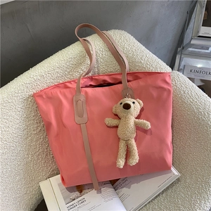 Pink large capacity tote bag with a cute beige plush bear pendant on a soft sofa