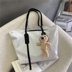 White large capacity tote bag with black straps and cute teddy bear charm on fashion magazines