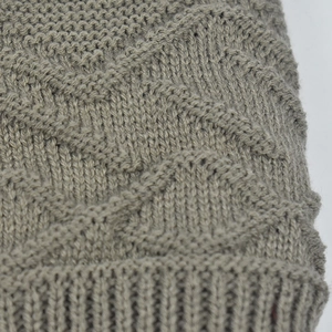 Macro detail of thick grey-brown knit texture with wavy pattern and ribbed edge on winter hat