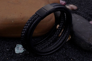 Macro detail of men's multi-layer black braided leather bracelet with matte magnetic clasp