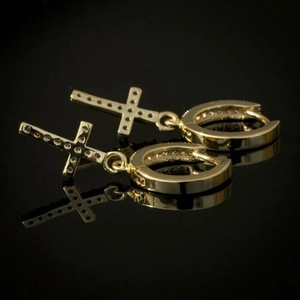 Macro detail of gold cross earrings featuring inlaid white zircon on a black reflective base